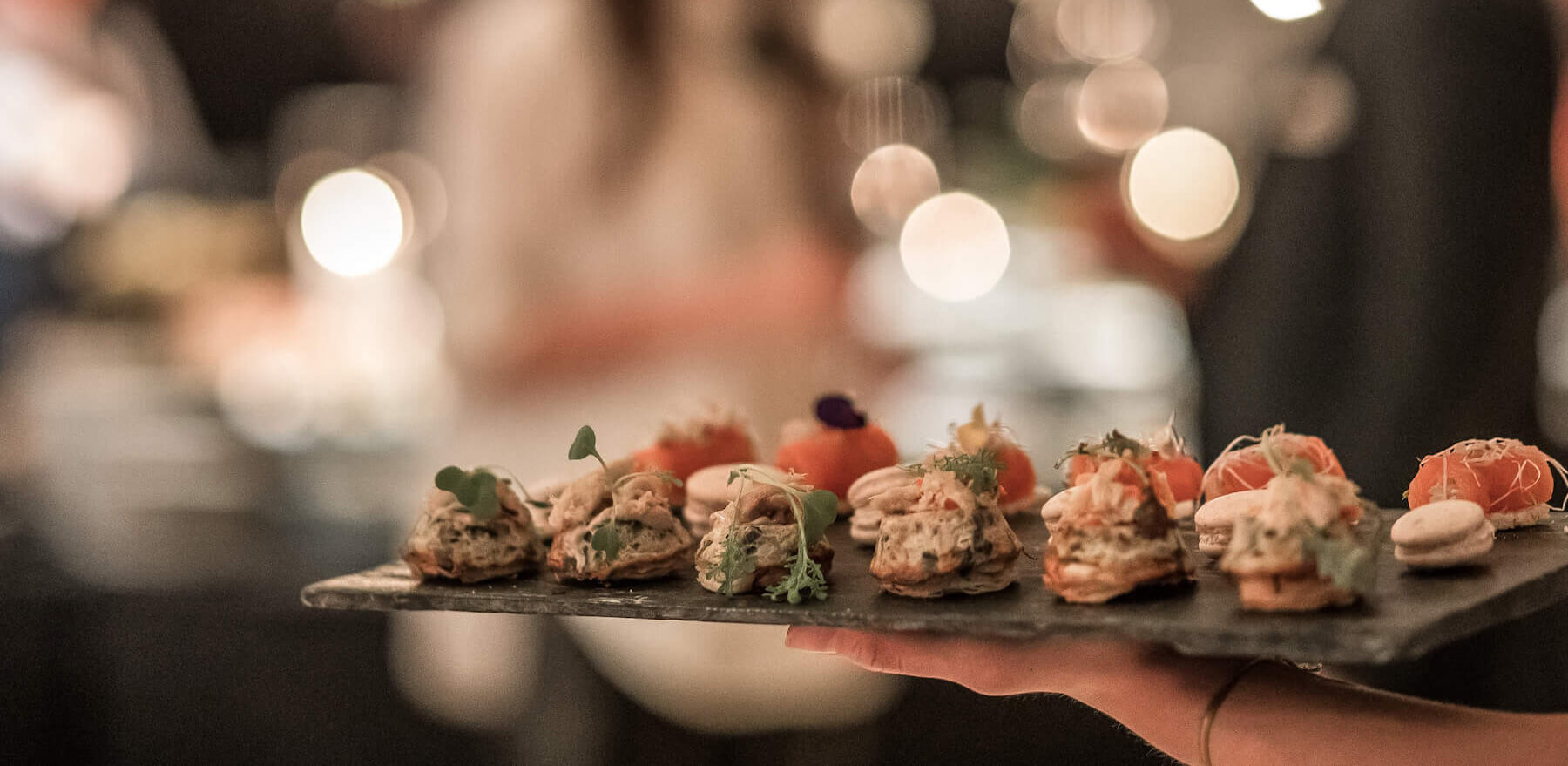 Close up of someone holding a wooden tray of hors doeuvres